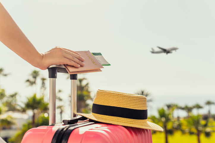 Woman with pink suitcase and passport with boarding pass standing on passengers ladder of airplane opposite sea with palm trees Tourism concept | Glam(グラム)