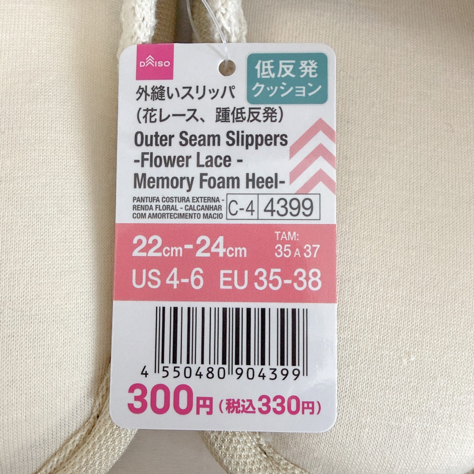 Tag showing product name 'Outer Seam Slippers - Flower Lace - Memory Foam Heel' with barcode and price (300 yen) on beige fabric.