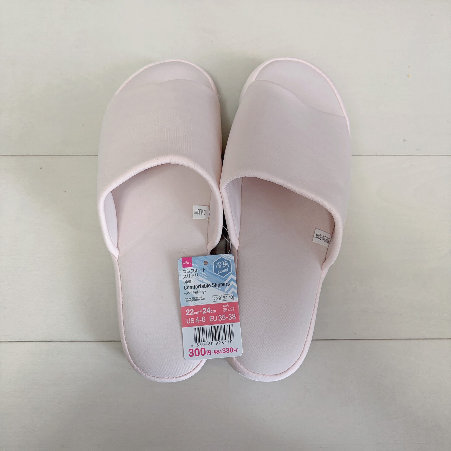 Pair of pastel pink slip-on indoor slippers viewed from above with price tag attached showing 300円 (tax included 330円)
