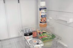 Inside a clean white refrigerator: a tall bottle of Japanese sesame dressing in a clear organizer shelf, with other packaged snacks on lower shelves.