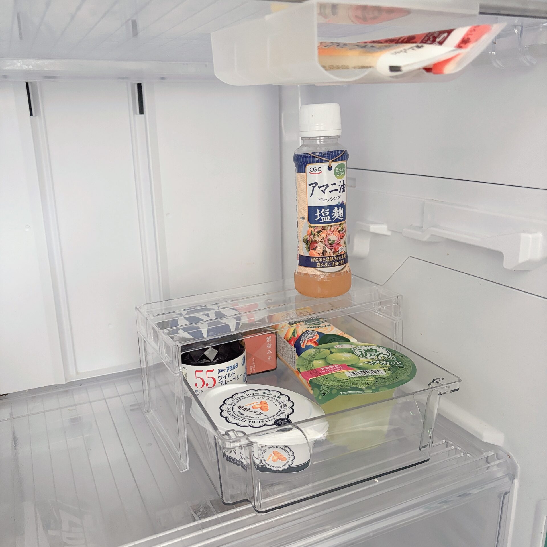 Inside a clean white refrigerator: a tall bottle of Japanese sesame dressing in a clear organizer shelf, with other packaged snacks on lower shelves.