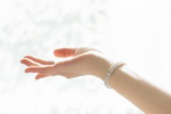 Outstretched hand with a diamond-studded bracelet on the wrist, against a bright white background.