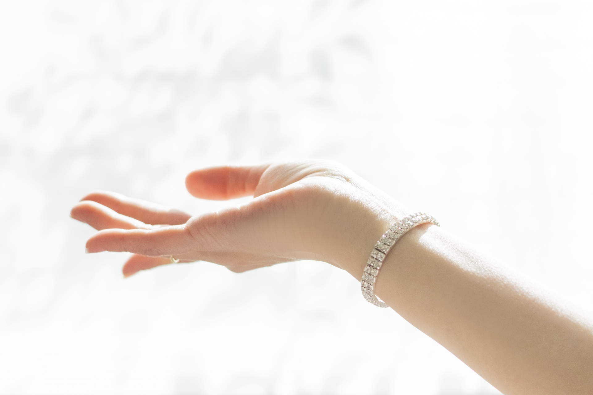 Outstretched hand with a diamond-studded bracelet on the wrist, against a bright white background.
