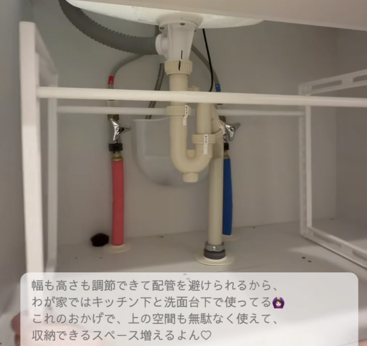 Under-sink view showing plumbing: beige P-trap, supply lines (red hot, blue cold) and drain connections beneath a kitchen sink.