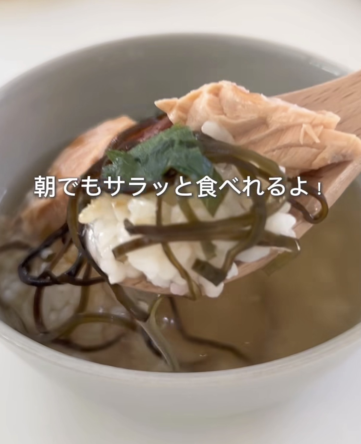 Screenshot | GLAM(グラム)|自分らしく生きる女性に、1日1GLAMを。 Bowl of clear broth with salmon, tofu, and wakame seaweed, held on a wooden spoon; a light, breakfast-friendly dish.