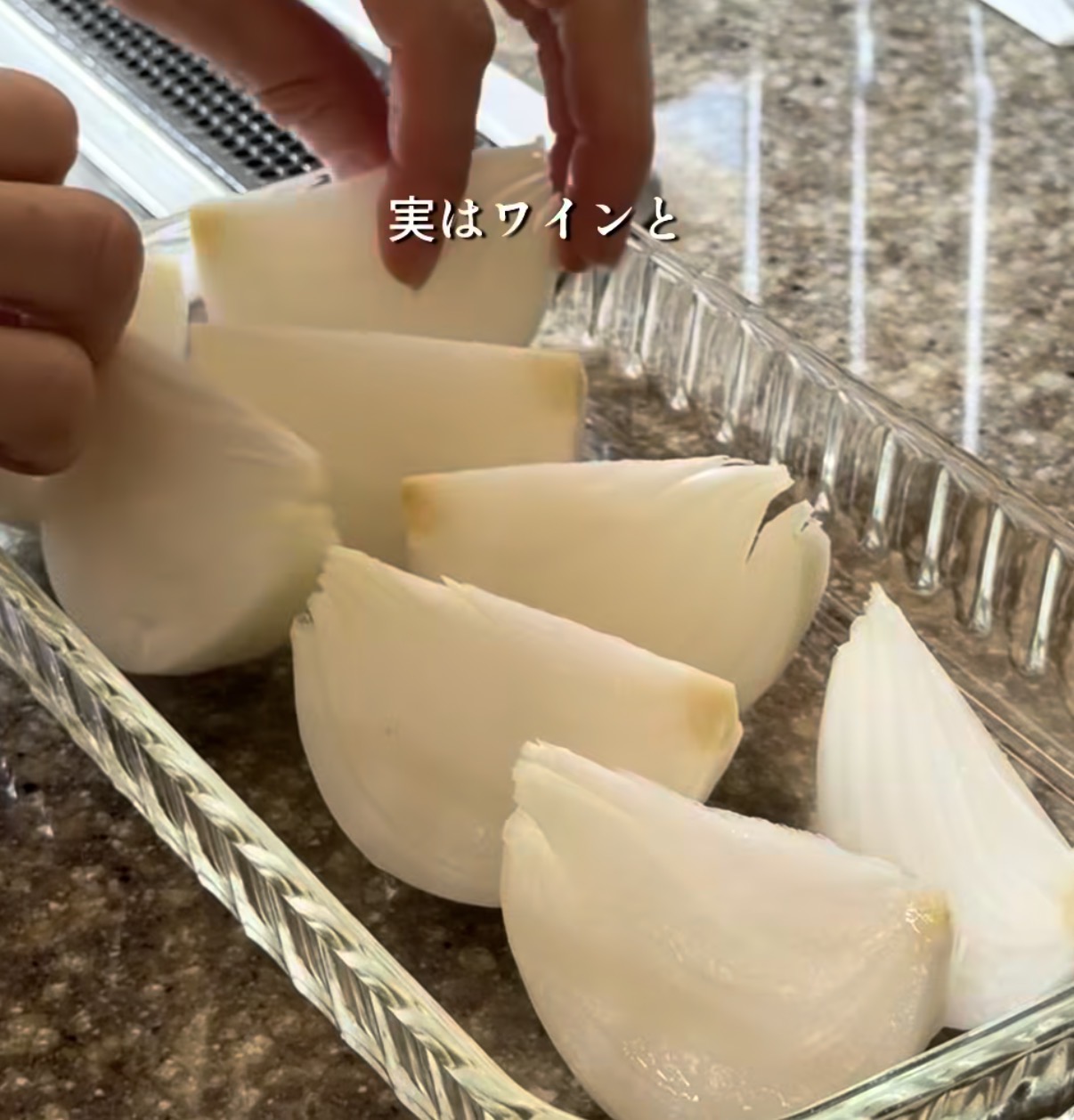 Hands slicing peeled white onions into wedges and placing them in a glass dish on a granite countertop.