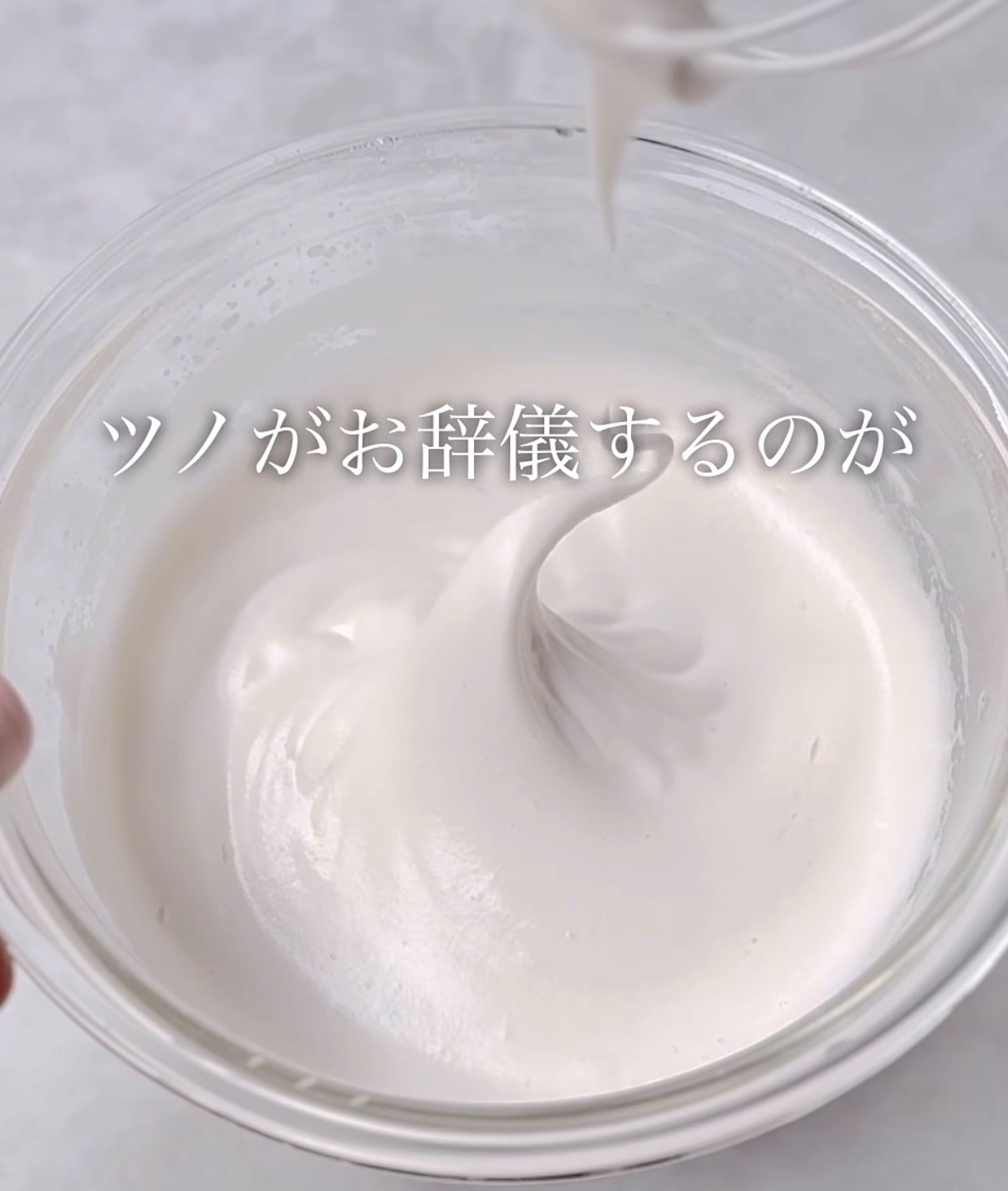 Whipped cream forming soft peaks in a glass bowl, whisk above; Japanese caption: ツノが お辞儀するのが