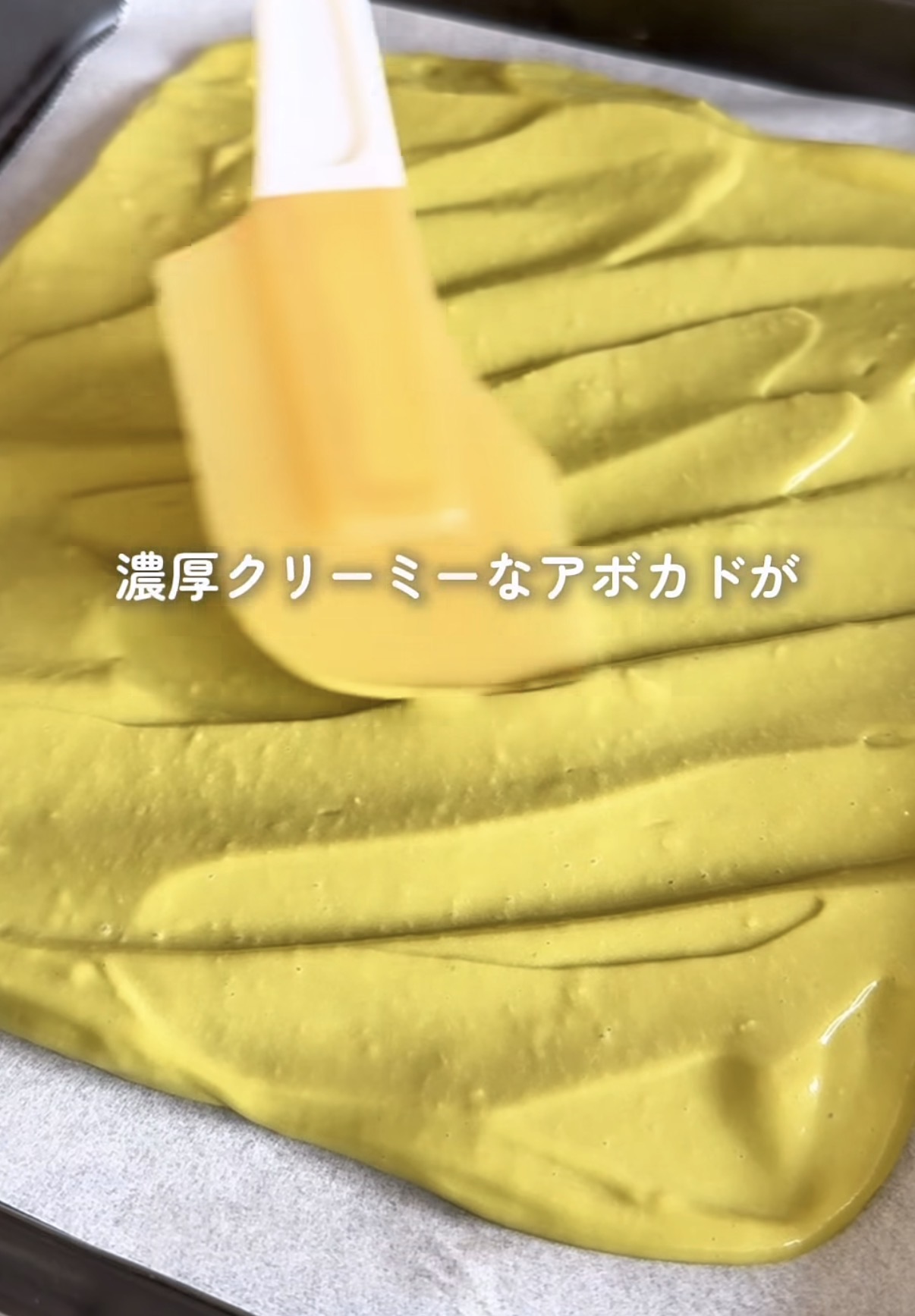 Creamy avocado spread being spread across a baking tray with a spatula in a kitchen setting