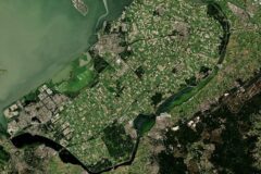 Aerial view of a river delta with patchwork green fields and urban areas along the banks.