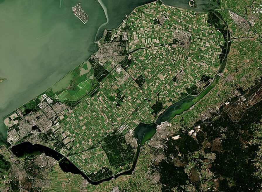 Aerial view of a river delta with patchwork green fields and urban areas along the banks.