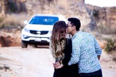 Couple kissing in an outdoor rocky area with a white SUV in the background.