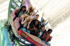 Group of friends on a looping roller coaster, screaming with excitement on a green track indoors
