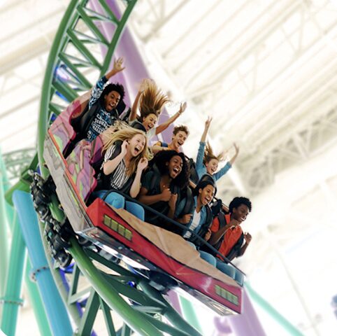 Group of friends on a looping roller coaster, screaming with excitement on a green track indoors