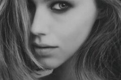 Close-up black-and-white portrait of a young woman with hair partly covering her face and a calm expression.